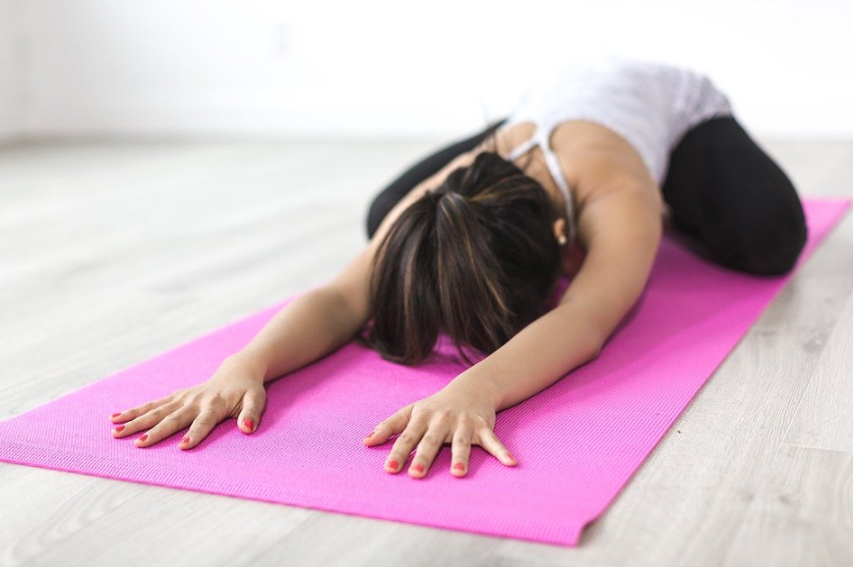 Eine Frau liegt auf einer pinken Yoga-Matte und macht eine Yoga-Übung